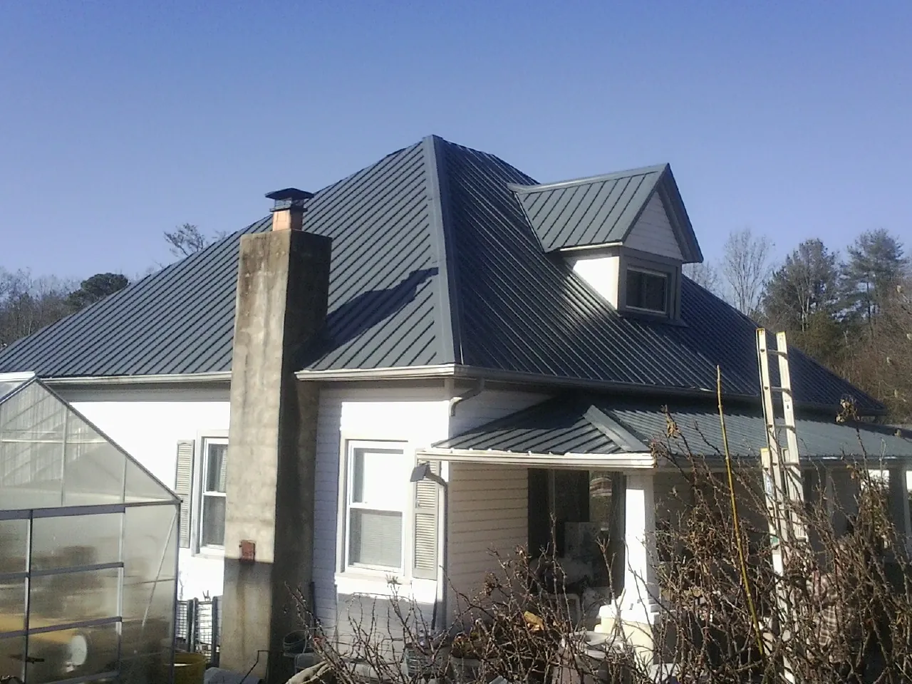 Dark blue standing seam metal roof on a white farmhouse with dormer — Slate & Tile Roof Repair by Roofing Brothers in Ponca