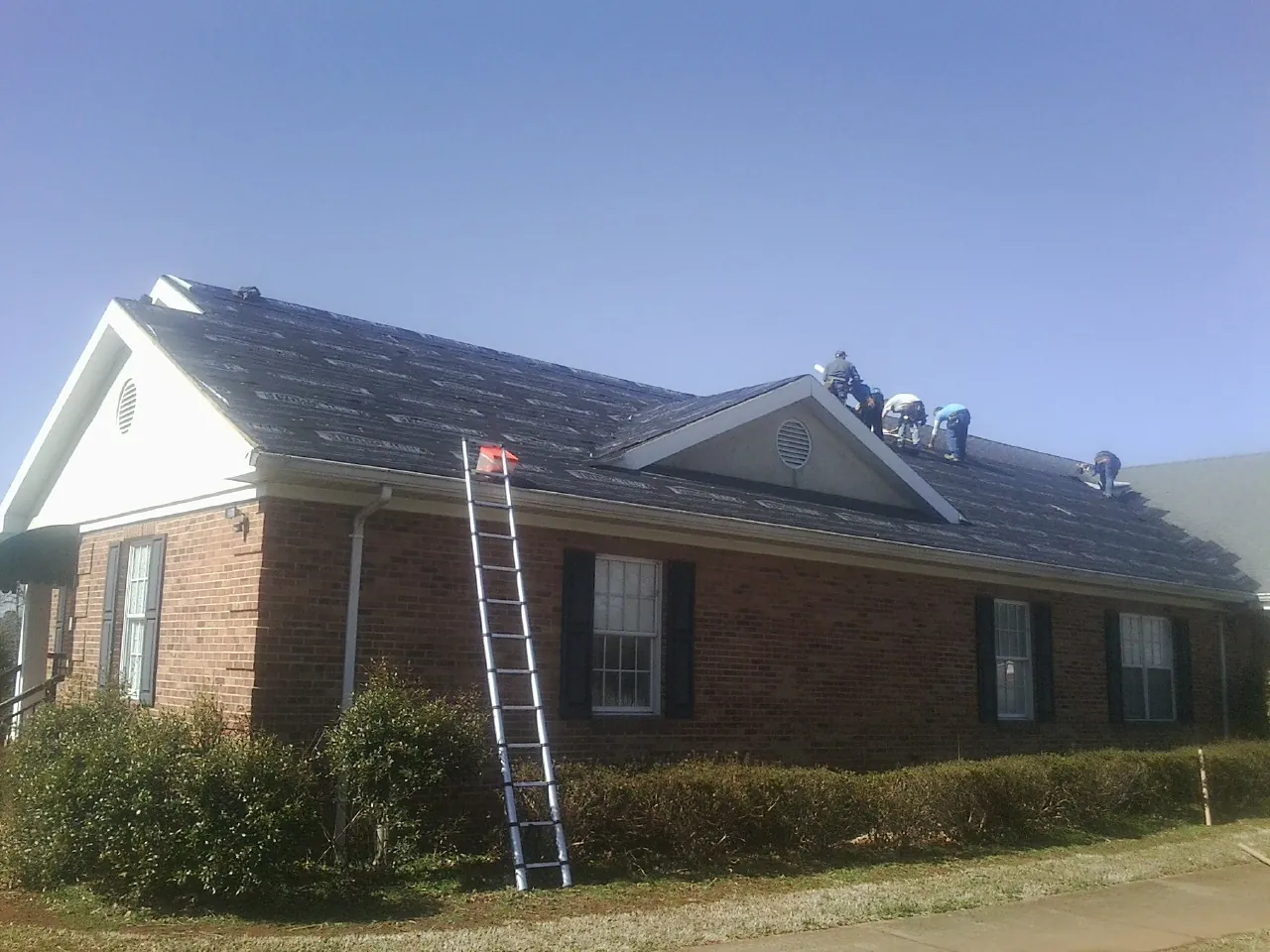 Crew tearing shingles off a brick ranch roof with a ladder set — Metal Roof Repair work by our crew in Ponca