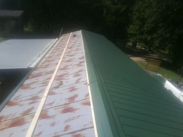 Old rusted panels beside newly installed green metal roofing — Wind Damage Roof Repair by Roofing Brothers in Ponca