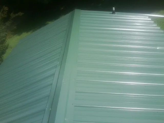 New green metal panels meeting at the ridge of a roof — Flat Roof Repair work by our crew in Ponca