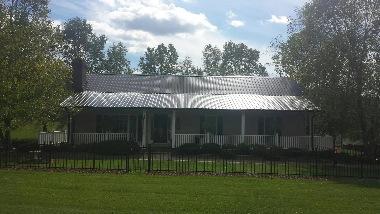 Gray metal roof on a brick ranch with a full width front porch — Gutter Guard Installation work by our crew in Ponca
