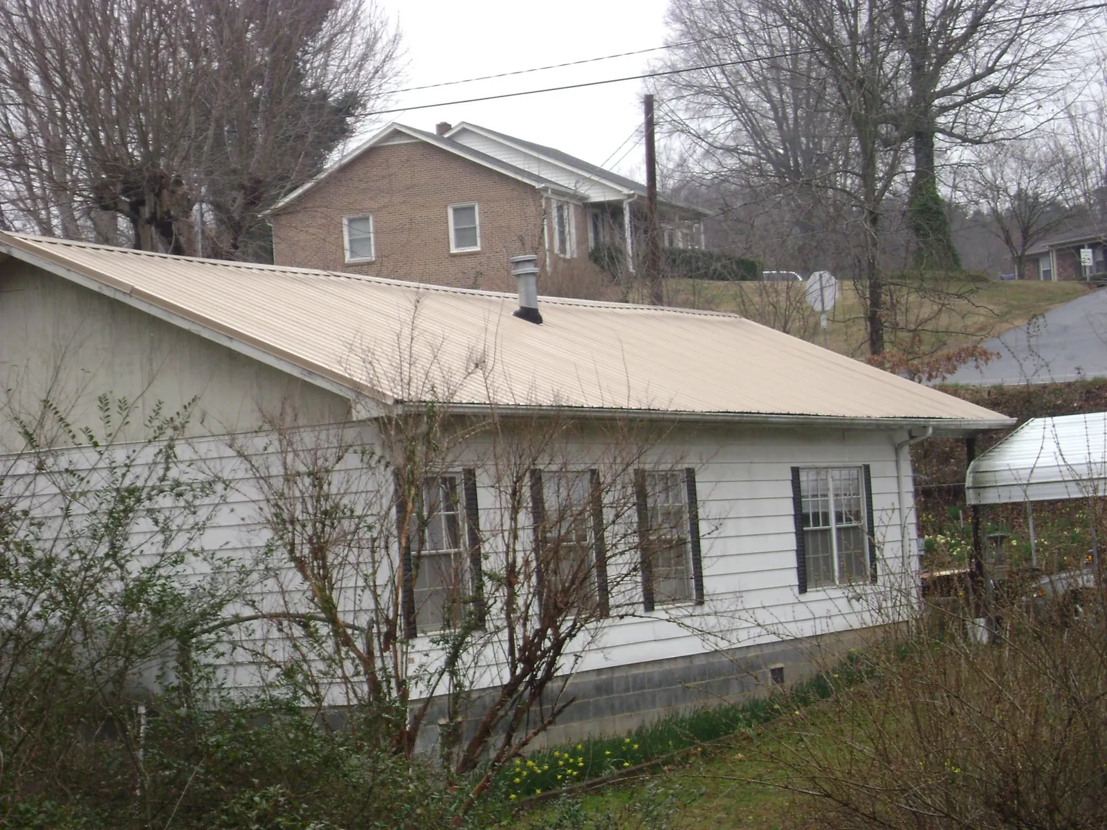 Tan metal roof on a white sided house set into a hillside — Commercial Roofing by Roofing Brothers in Ponca