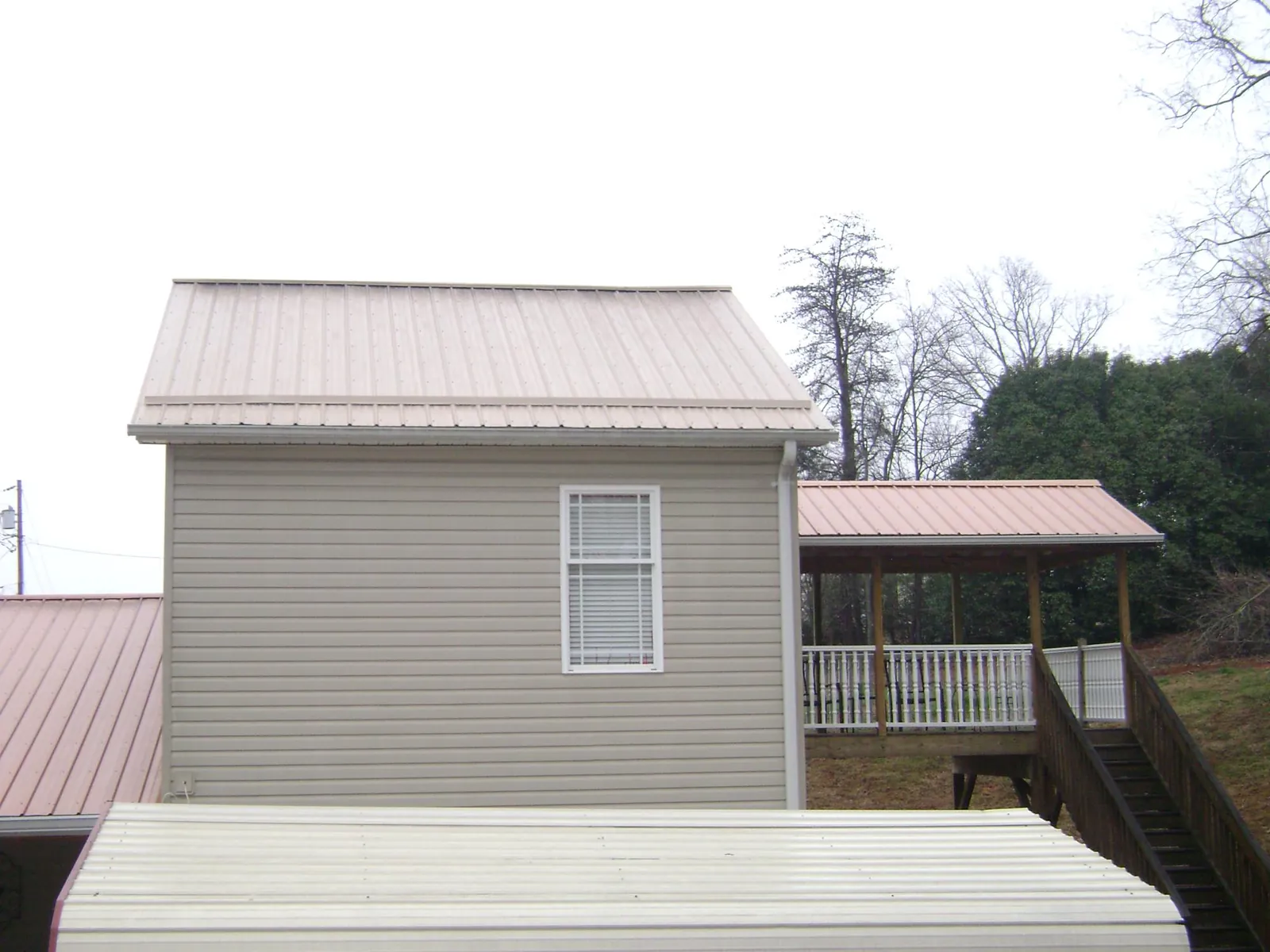 Tan metal roofs on a two story addition and attached porch, from a Roof Replacement job in Ponca